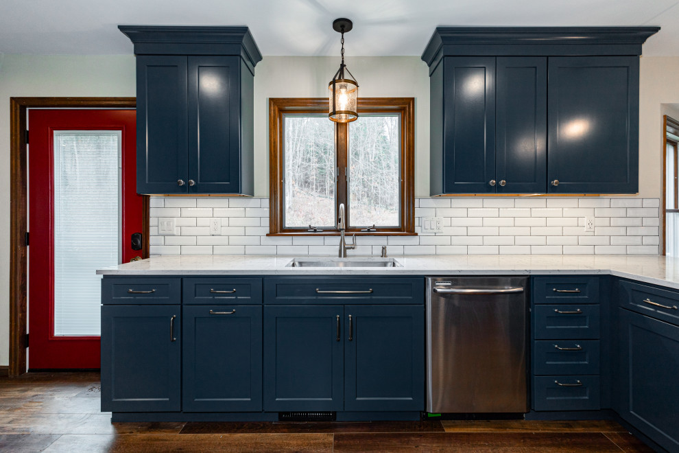 Design ideas for a mid-sized country l-shaped eat-in kitchen in New York with an undermount sink, shaker cabinets, blue cabinets, quartz benchtops, white splashback, subway tile splashback, stainless steel appliances, dark hardwood floors, a peninsula, brown floor and white benchtop.