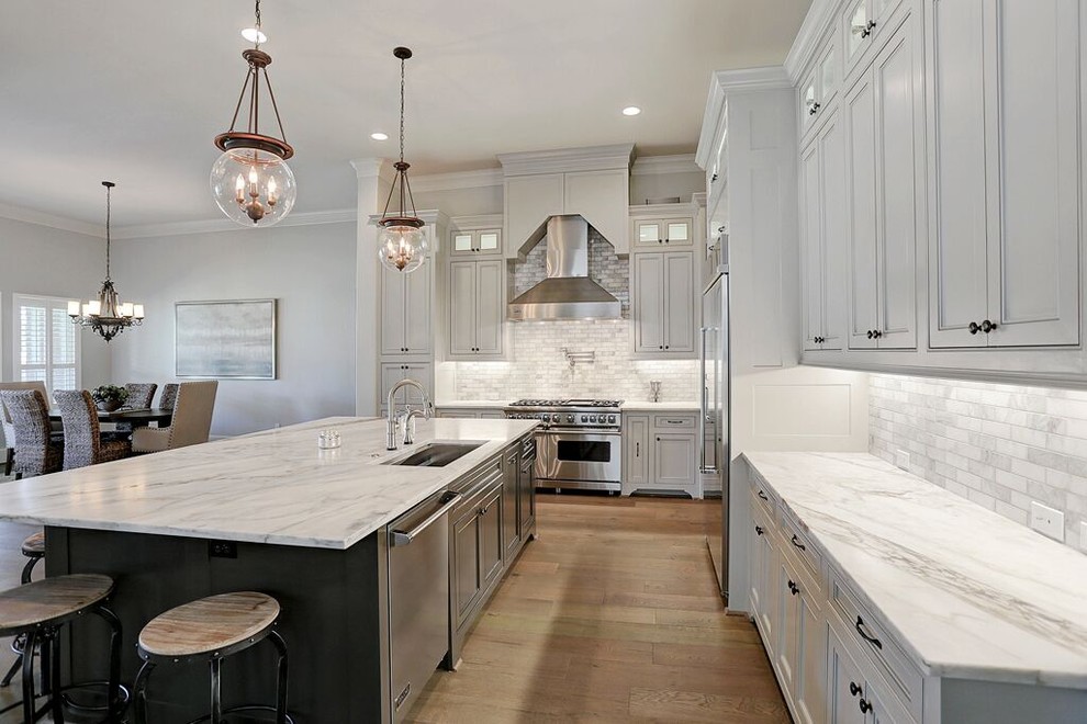 This is an example of a large transitional l-shaped eat-in kitchen in Houston with an undermount sink, shaker cabinets, white cabinets, marble benchtops, white splashback, marble splashback, stainless steel appliances, medium hardwood floors and with island.