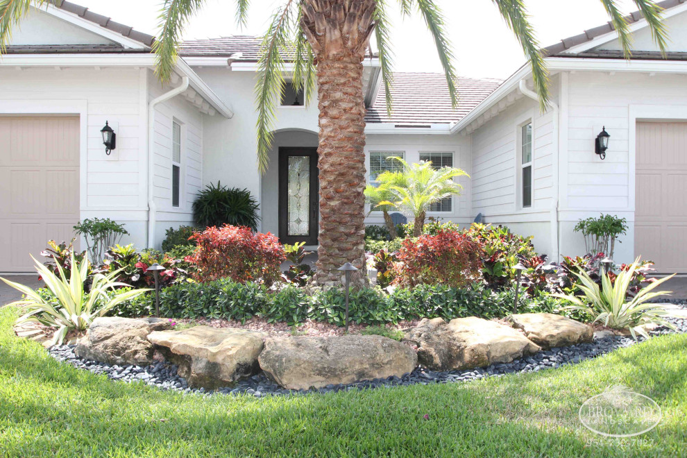 This is an example of a mid-sized tropical front yard driveway in Miami with with flowerbed and natural stone pavers.