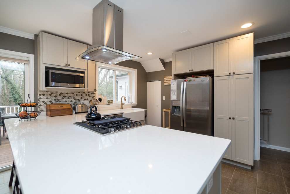 Example of a mid-sized transitional l-shaped laminate floor open concept kitchen design in DC Metro with a farmhouse sink, shaker cabinets, white cabinets, quartz countertops, gray backsplash, porcelain backsplash, stainless steel appliances and a peninsula