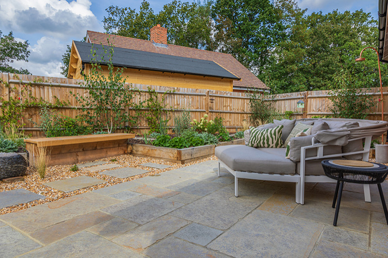 Small rural back full sun garden seating for summer in Surrey with natural stone paving and a wood fence.