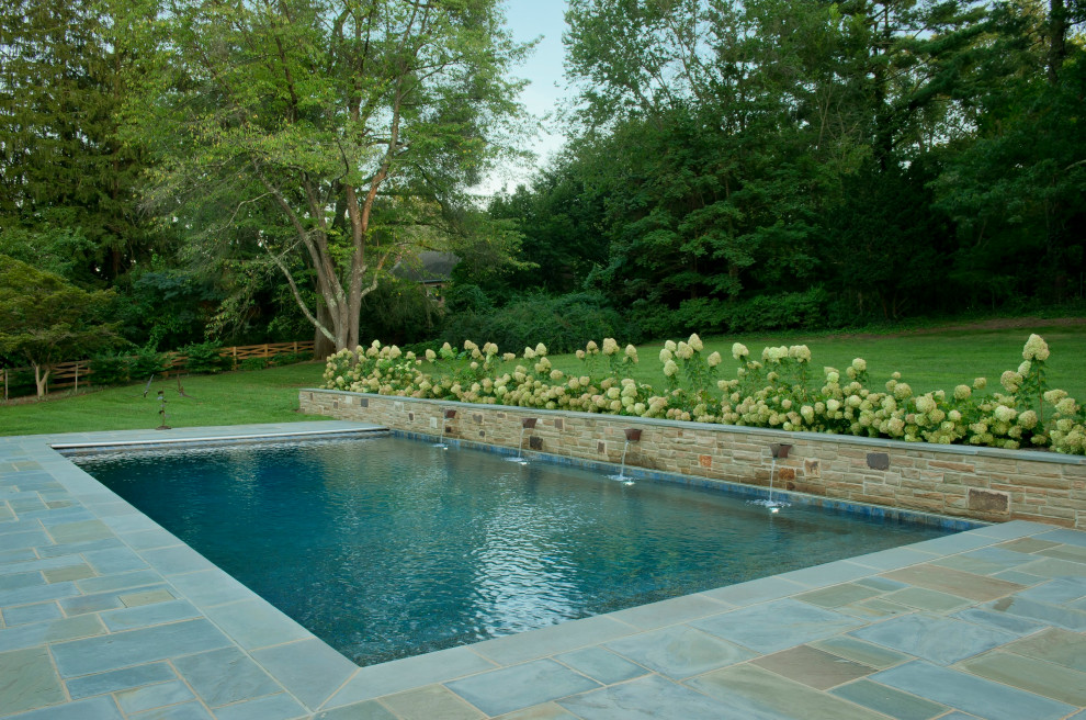Photo of a traditional back rectangular infinity swimming pool in Baltimore with a water feature and natural stone paving.