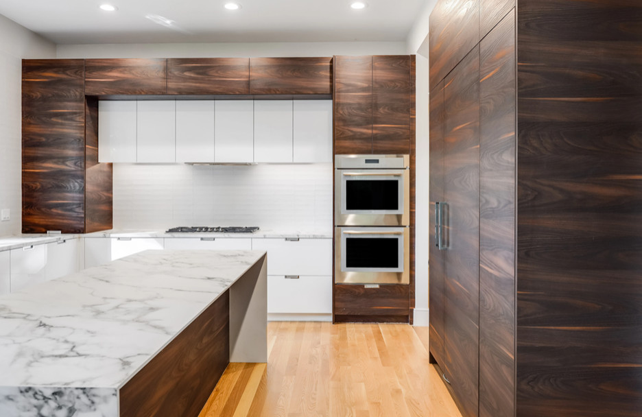 Photo of a contemporary l-shaped eat-in kitchen in Boston with an undermount sink, flat-panel cabinets, quartz benchtops, white splashback, medium hardwood floors, with island and white benchtop.