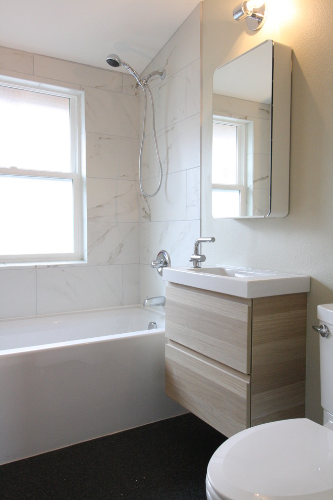 Inspiration for a small modern 3/4 bathroom in Portland with flat-panel cabinets, light wood cabinets, an alcove tub, a shower/bathtub combo, a two-piece toilet, white tile, marble, grey walls, laminate floors, an integrated sink, quartzite benchtops, black floor and an open shower.