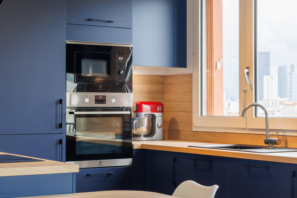 Photo of a small modern u-shaped open plan kitchen in Paris with a submerged sink, recessed-panel cabinets, blue cabinets, wood worktops, beige splashback, wood splashback, integrated appliances, cement flooring, no island, blue floors and beige worktops.