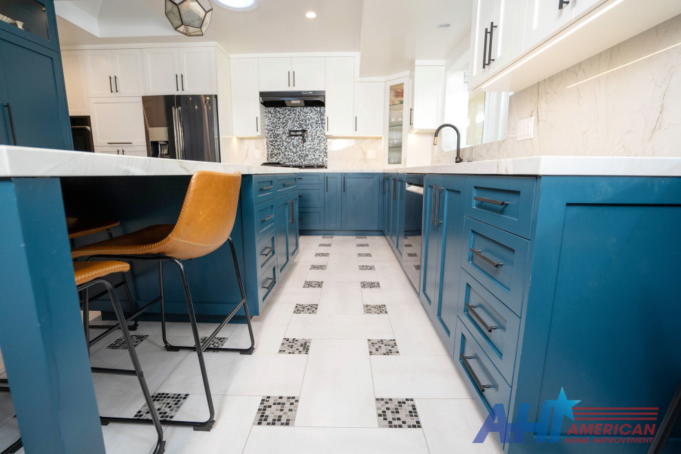 Inspiration for a mid-sized modern u-shaped porcelain tile, multicolored floor and tray ceiling open concept kitchen remodel in Los Angeles with a drop-in sink, raised-panel cabinets, blue cabinets, marble countertops, white backsplash, marble backsplash, stainless steel appliances, an island and white countertops