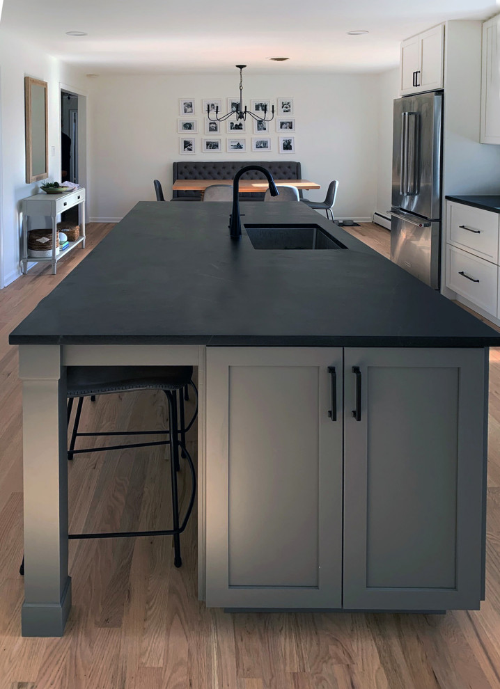 Photo of a large contemporary open plan kitchen in Philadelphia with an undermount sink, shaker cabinets, grey cabinets, soapstone benchtops, grey splashback, ceramic splashback, stainless steel appliances, light hardwood floors, with island, brown floor and black benchtop.
