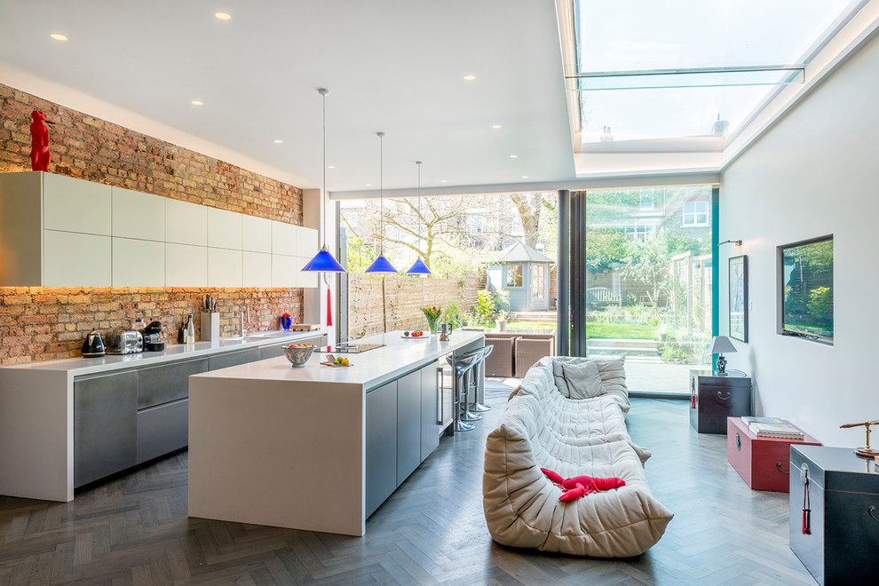 Photo of a large contemporary single-wall open plan kitchen in London with an integrated sink, flat-panel cabinets, grey cabinets, solid surface benchtops, pink splashback, brick splashback, stainless steel appliances, dark hardwood floors, with island and grey floor.
