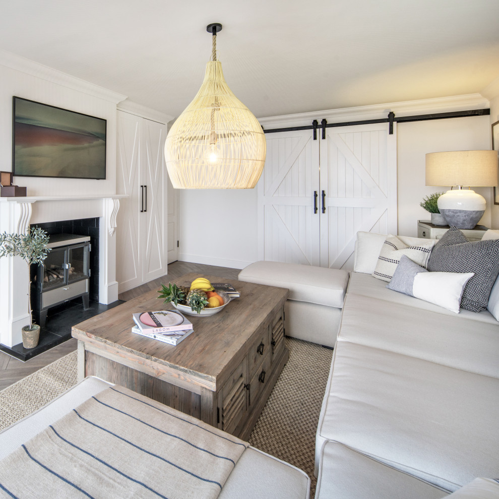 This is an example of a beach style cream and black enclosed living room curtain in Other with a home bar, white walls, laminate floors, a wood burning stove, a wooden fireplace surround, a wall mounted tv and brown floors.