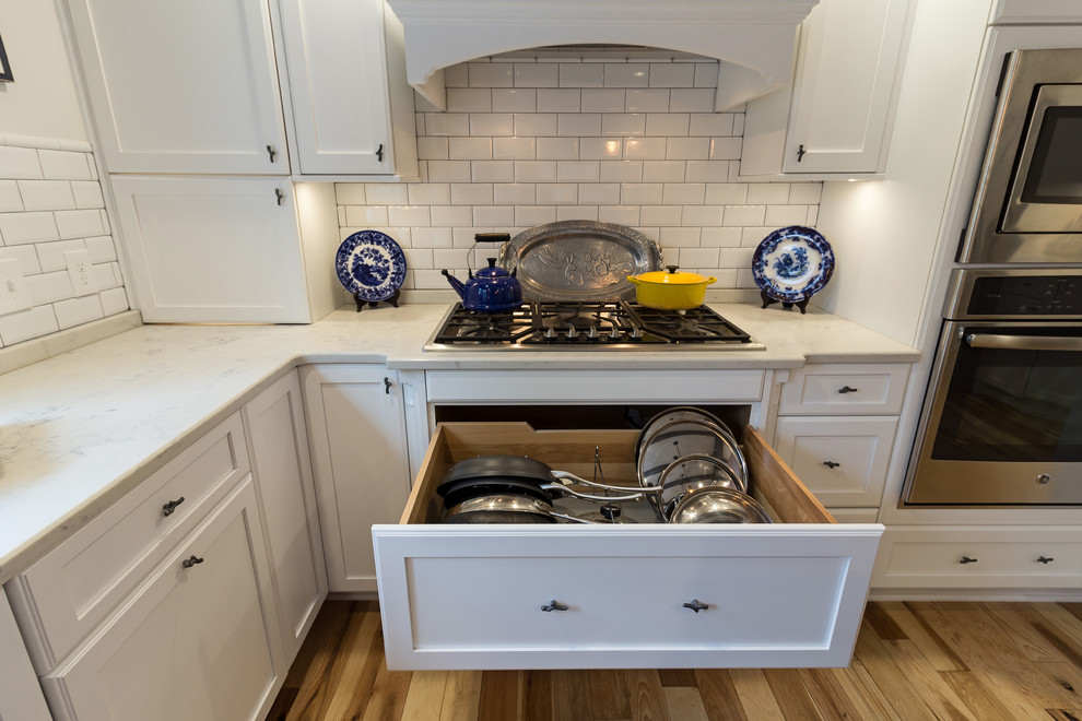 Example of a large transitional u-shaped medium tone wood floor and brown floor enclosed kitchen design with an undermount sink, shaker cabinets, white cabinets, quartzite countertops, white backsplash, subway tile backsplash, stainless steel appliances and an island