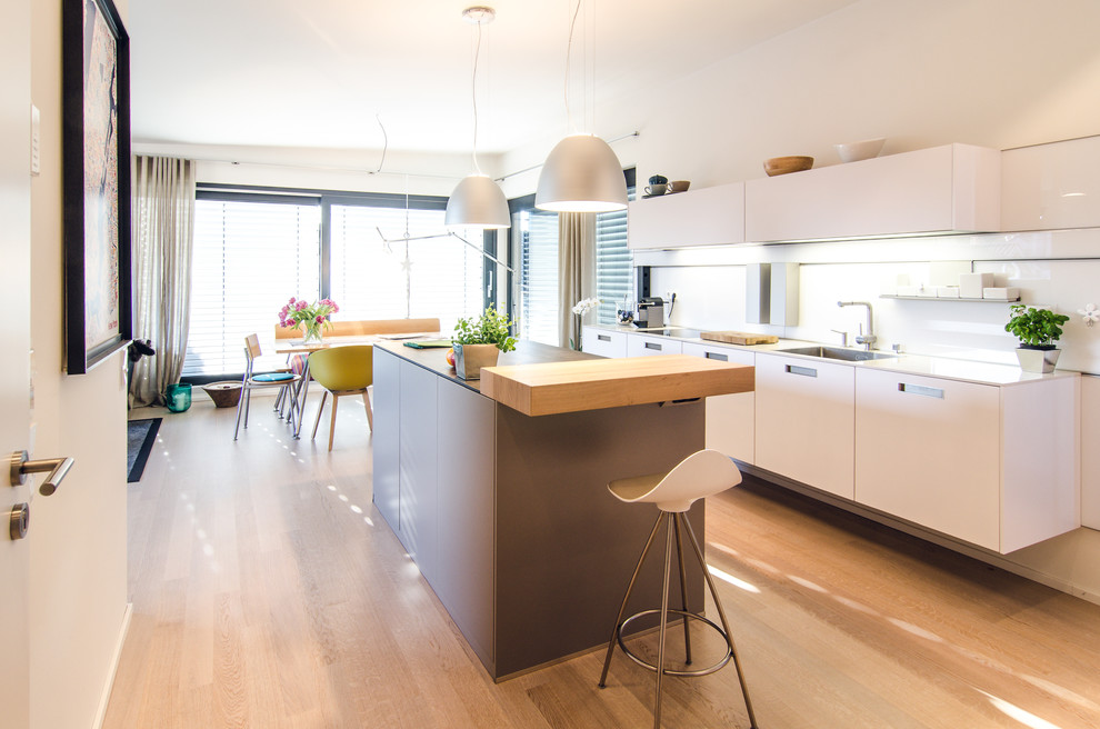 Inspiration for a mid-sized contemporary galley eat-in kitchen in Frankfurt with with island, flat-panel cabinets, white splashback, light hardwood floors and beige floor.