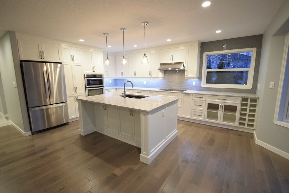 Inspiration for a transitional l-shaped vinyl floor eat-in kitchen remodel in Edmonton with a double-bowl sink, shaker cabinets, white cabinets, quartz countertops, gray backsplash, glass tile backsplash, stainless steel appliances and an island