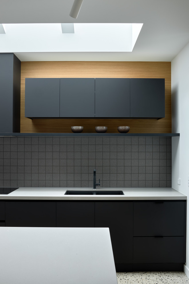 Inspiration for a large contemporary kitchen in Melbourne with flat-panel cabinets, black cabinets, solid surface benchtops, grey splashback, mosaic tile splashback, black appliances, concrete floors, with island, multi-coloured floor and grey benchtop.