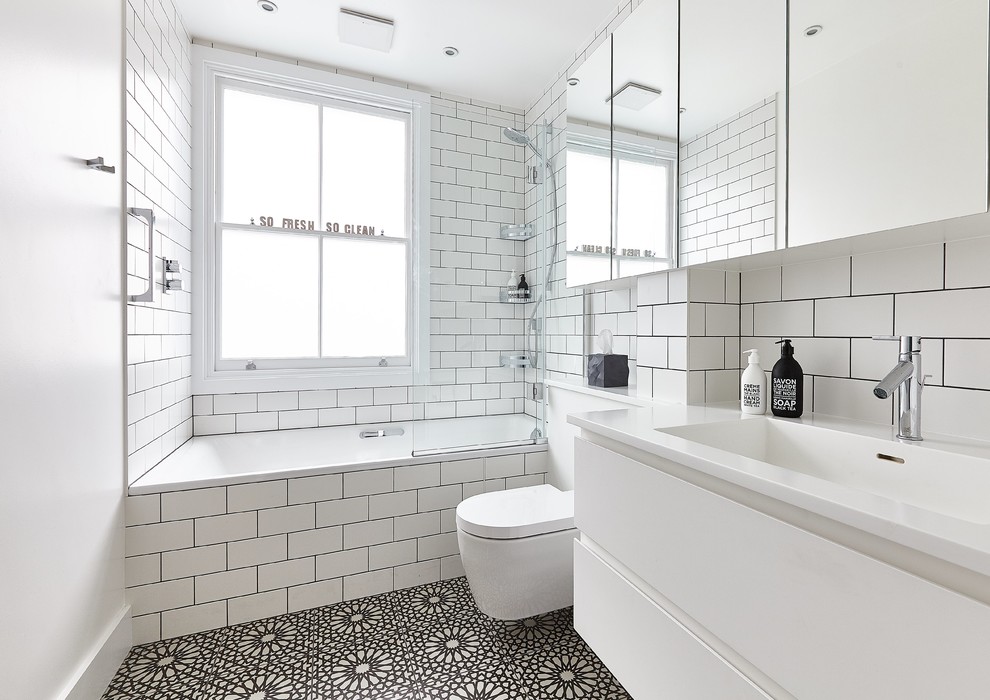 Inspiration for a contemporary 3/4 bathroom in London with flat-panel cabinets, white cabinets, an alcove tub, a shower/bathtub combo, a wall-mount toilet, white tile, subway tile, white walls, cement tiles, an integrated sink, black floor and an open shower.