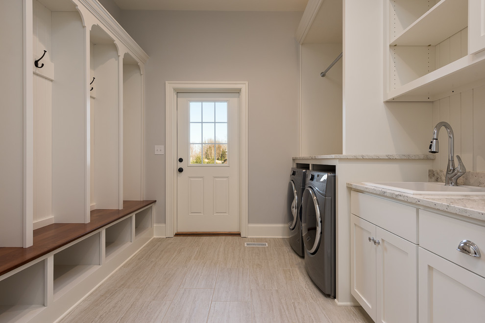 This is an example of a large transitional galley utility room in Other with a drop-in sink, shaker cabinets, white cabinets, limestone benchtops, grey walls, porcelain floors, a side-by-side washer and dryer and beige floor.