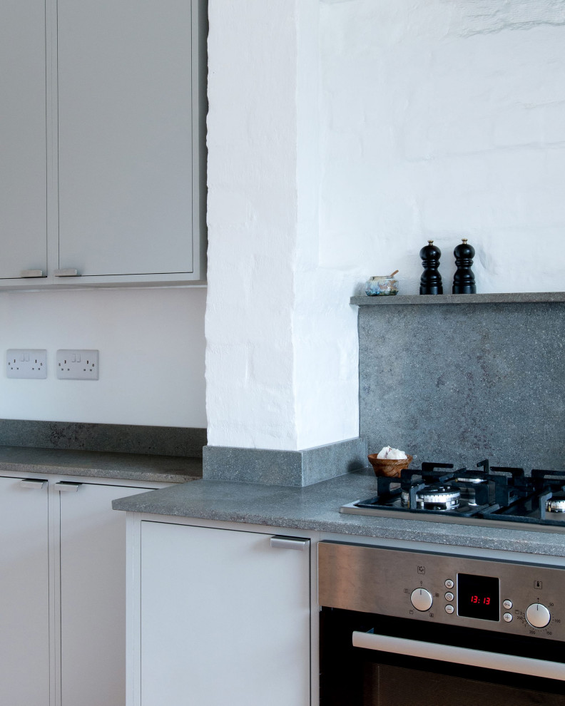 Design ideas for a small contemporary l-shaped kitchen/diner in London with a double-bowl sink, flat-panel cabinets, grey cabinets, limestone worktops, grey splashback, limestone splashback, stainless steel appliances, cork flooring, no island, grey worktops and a chimney breast.