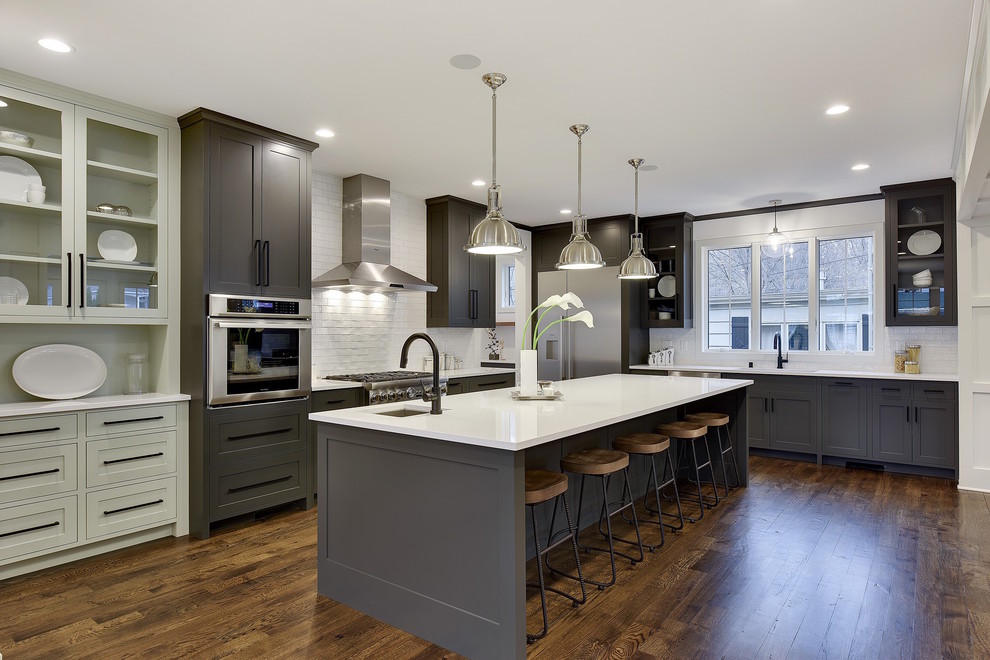 Transitional l-shaped kitchen in Minneapolis with stainless steel appliances, with island, brown floor, white benchtop, an undermount sink, shaker cabinets, grey cabinets, white splashback and medium hardwood floors.