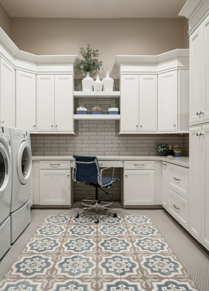 Klassisk inredning av en stor vita u-formad vitt tvättstuga enbart för tvätt, med en rustik diskho, luckor med profilerade fronter, vita skåp, bänkskiva i kvarts, grått stänkskydd, stänkskydd i porslinskakel, grå väggar, klinkergolv i keramik, en tvättmaskin och torktumlare bredvid varandra och blått golv