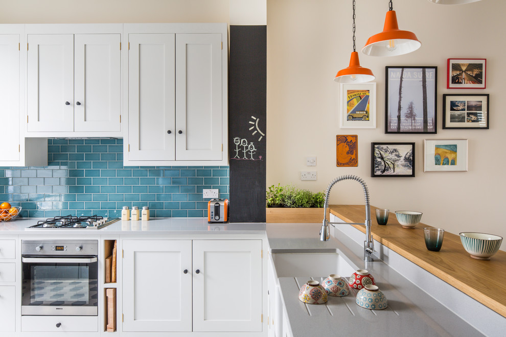 This is an example of a small transitional l-shaped kitchen in London with a farmhouse sink, shaker cabinets, white cabinets, quartz benchtops, blue splashback, subway tile splashback, stainless steel appliances, ceramic floors and multi-coloured floor.