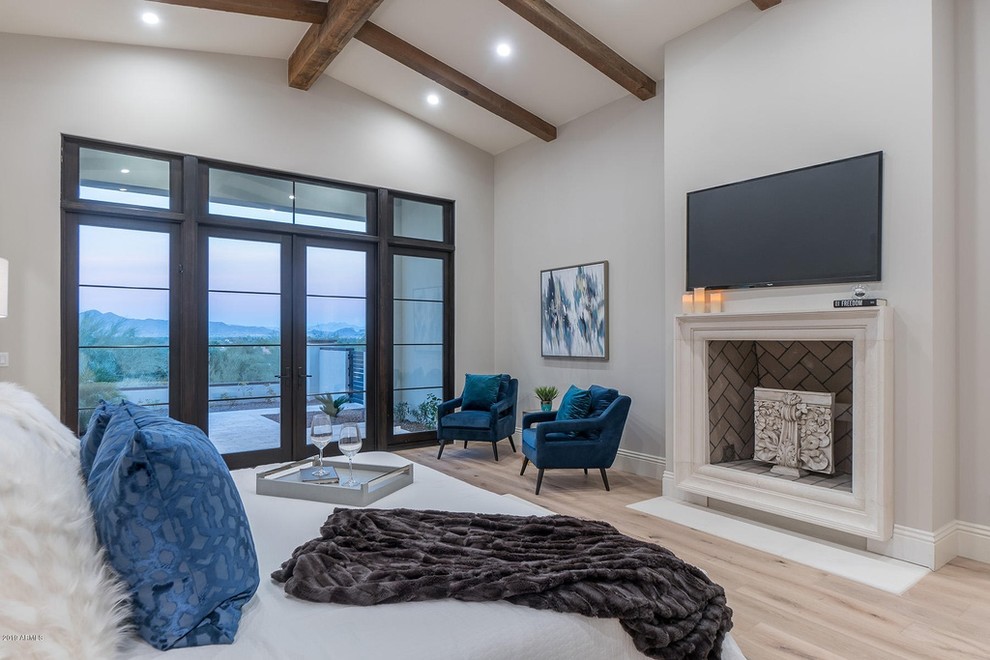 Inspiration for a large contemporary master bedroom in Phoenix with beige walls, light hardwood floors, a standard fireplace, a wood fireplace surround and beige floor.