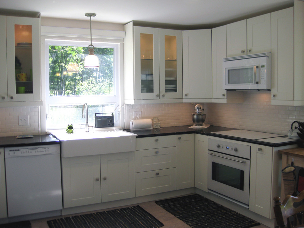 This is an example of a transitional u-shaped eat-in kitchen in Milwaukee with a farmhouse sink, recessed-panel cabinets, white cabinets, quartz benchtops, white splashback, subway tile splashback and white appliances.
