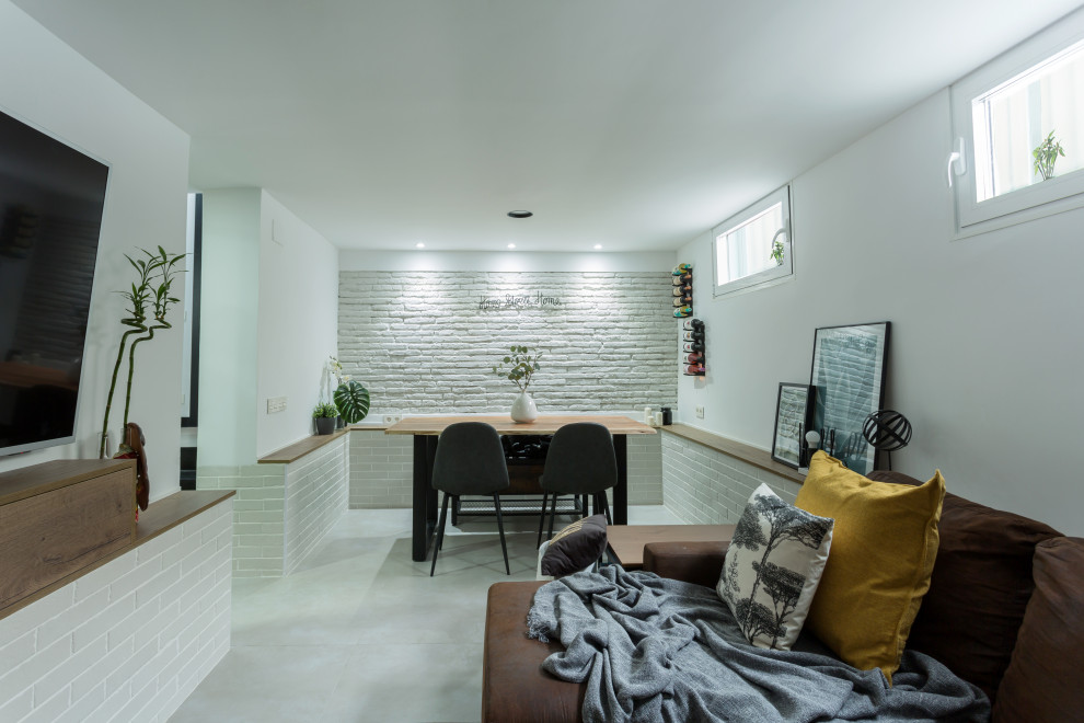 Small industrial enclosed living room in Madrid with a home bar, white walls, porcelain floors, a hanging fireplace, a wall-mounted tv, grey floor and brick walls.
