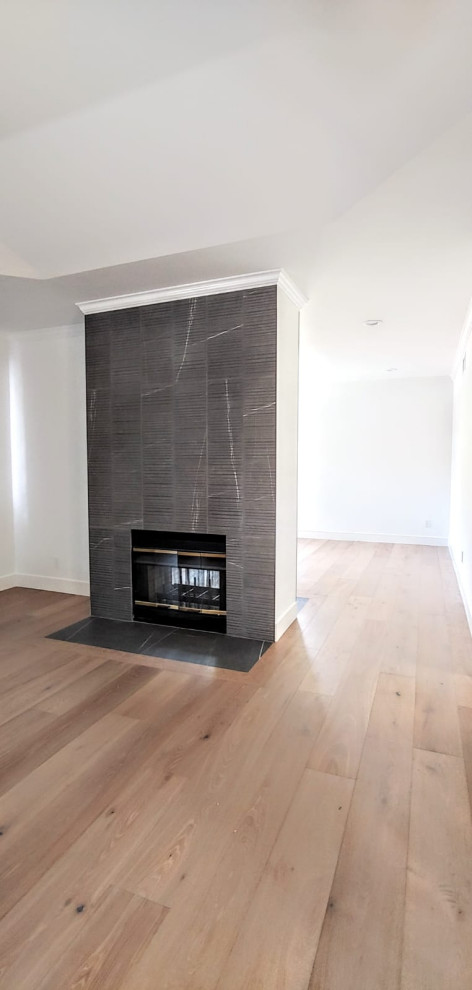 Photo of a large modern master bedroom in Los Angeles with white walls, medium hardwood flooring, a two-sided fireplace, a tiled fireplace surround and beige floors.