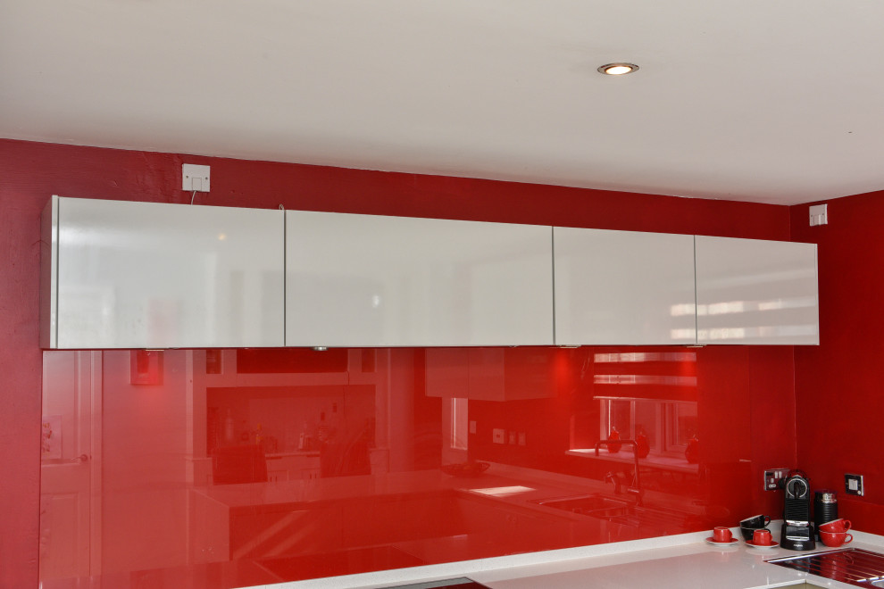 Inspiration for a mid-sized modern u-shaped eat-in kitchen in Cheshire with a single-bowl sink, glass-front cabinets, white cabinets, granite benchtops, red splashback, glass sheet splashback, panelled appliances, porcelain floors, a peninsula, grey floor and white benchtop.