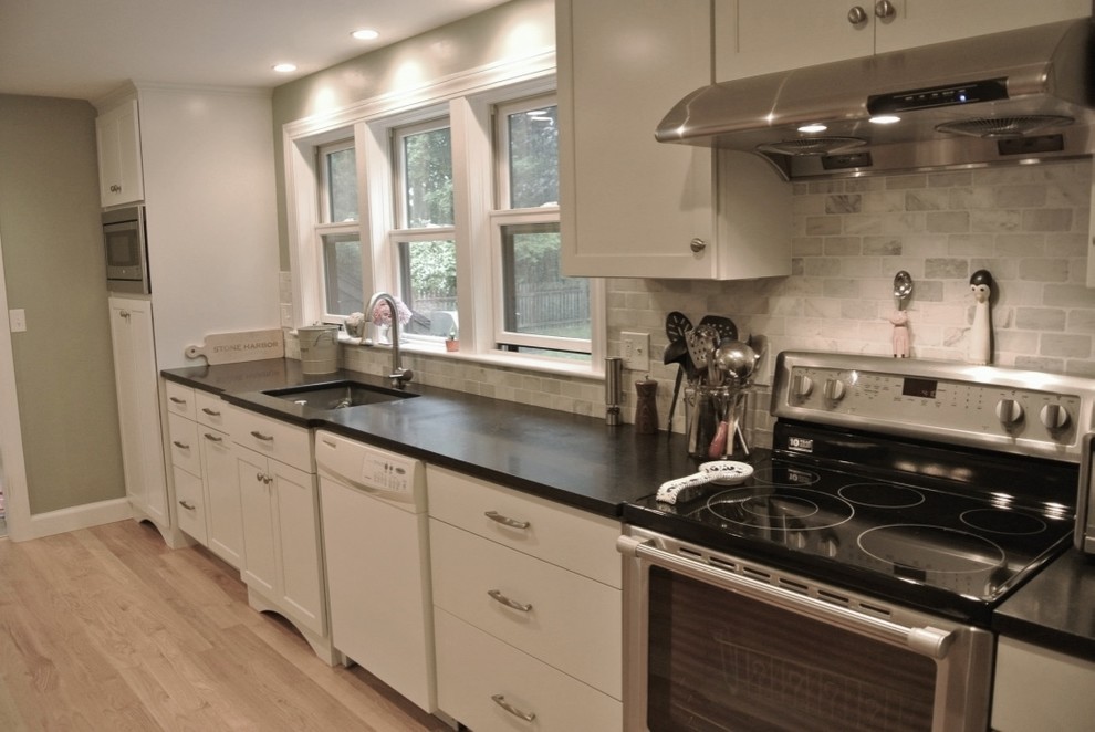 Example of a transitional u-shaped light wood floor eat-in kitchen design in Boston with an undermount sink, shaker cabinets, white cabinets, beige backsplash, porcelain backsplash, stainless steel appliances, a peninsula and black countertops