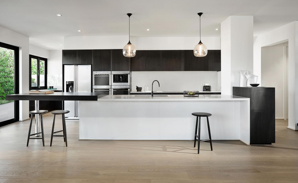 Design ideas for an expansive contemporary galley kitchen in Melbourne with an undermount sink, flat-panel cabinets, black cabinets, white splashback, stainless steel appliances, medium hardwood floors, a peninsula, beige floor and white benchtop.