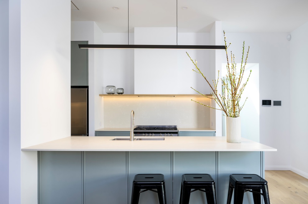 Inspiration for a mid-sized modern galley eat-in kitchen in Newcastle - Maitland with an undermount sink, shaker cabinets, blue cabinets, quartz benchtops, white splashback, engineered quartz splashback, stainless steel appliances, light hardwood floors, a peninsula and white benchtop.