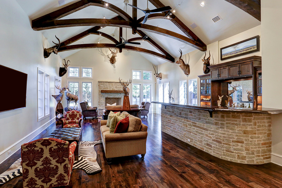 Design ideas for a large traditional open concept living room in Houston with a home bar, beige walls, medium hardwood floors, a standard fireplace, a brick fireplace surround, a wall-mounted tv, brown floor and exposed beam.