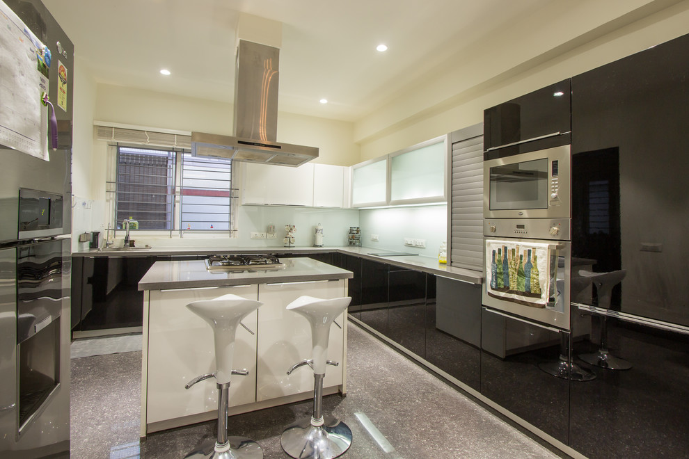 This is an example of a contemporary l-shaped kitchen in Bengaluru with flat-panel cabinets, black cabinets, glass sheet splashback, stainless steel appliances and with island.