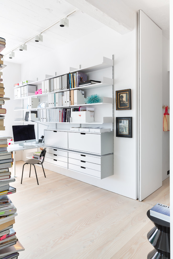 Photo of a scandinavian home studio in London with white walls, light hardwood floors and a built-in desk.