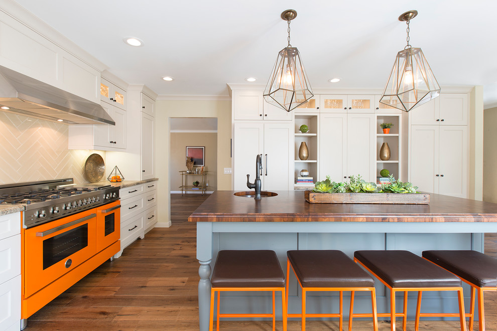 Example of a transitional dark wood floor kitchen design in Orange County with an undermount sink, flat-panel cabinets, white cabinets, wood countertops, beige backsplash, ceramic backsplash, colored appliances and an island