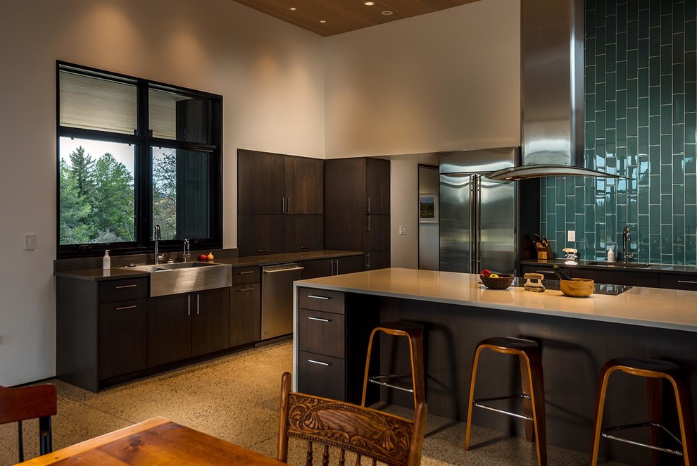 Example of a trendy eat-in kitchen design with a farmhouse sink, flat-panel cabinets, dark wood cabinets, green backsplash, ceramic backsplash, stainless steel appliances and an island