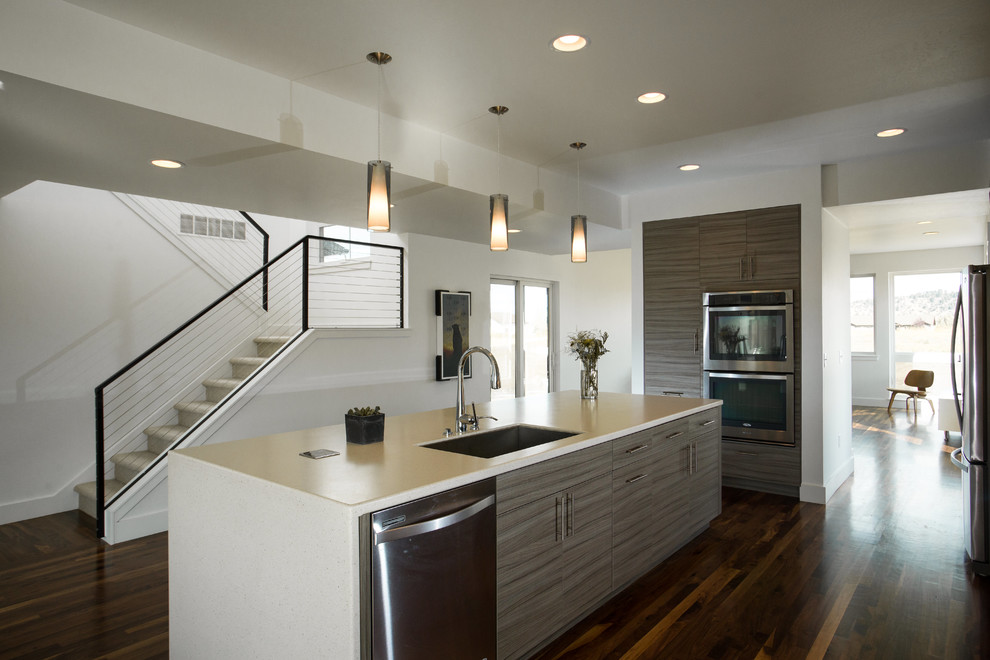 Mid-sized transitional l-shaped dark wood floor eat-in kitchen photo with a single-bowl sink, flat-panel cabinets, gray cabinets, solid surface countertops, white backsplash, porcelain backsplash, stainless steel appliances and an island