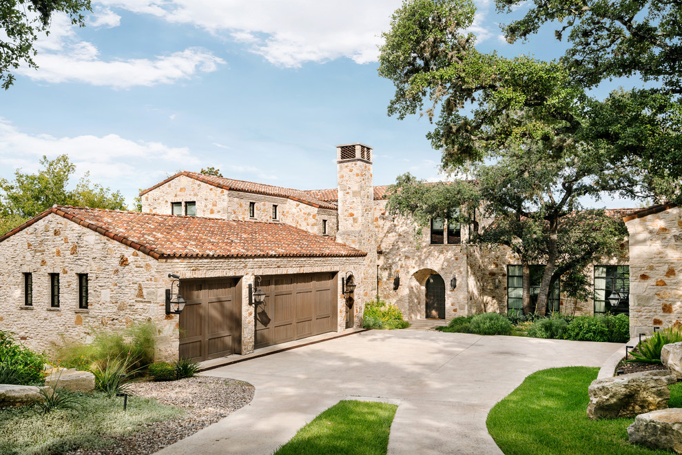 Photo of a mediterranean two-storey multi-coloured house exterior in Austin with stone veneer, a gable roof and a tile roof.