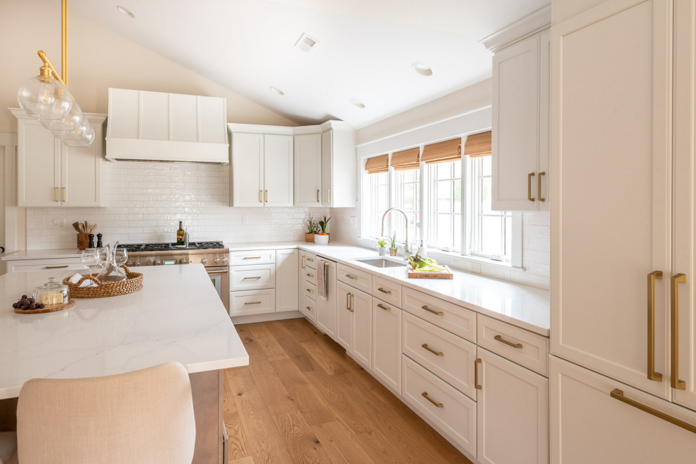 Eat-in kitchen - huge transitional l-shaped light wood floor, brown floor and vaulted ceiling eat-in kitchen idea in Boston with an undermount sink, shaker cabinets, white cabinets, quartz countertops, white backsplash, ceramic backsplash, paneled appliances, an island and white countertops