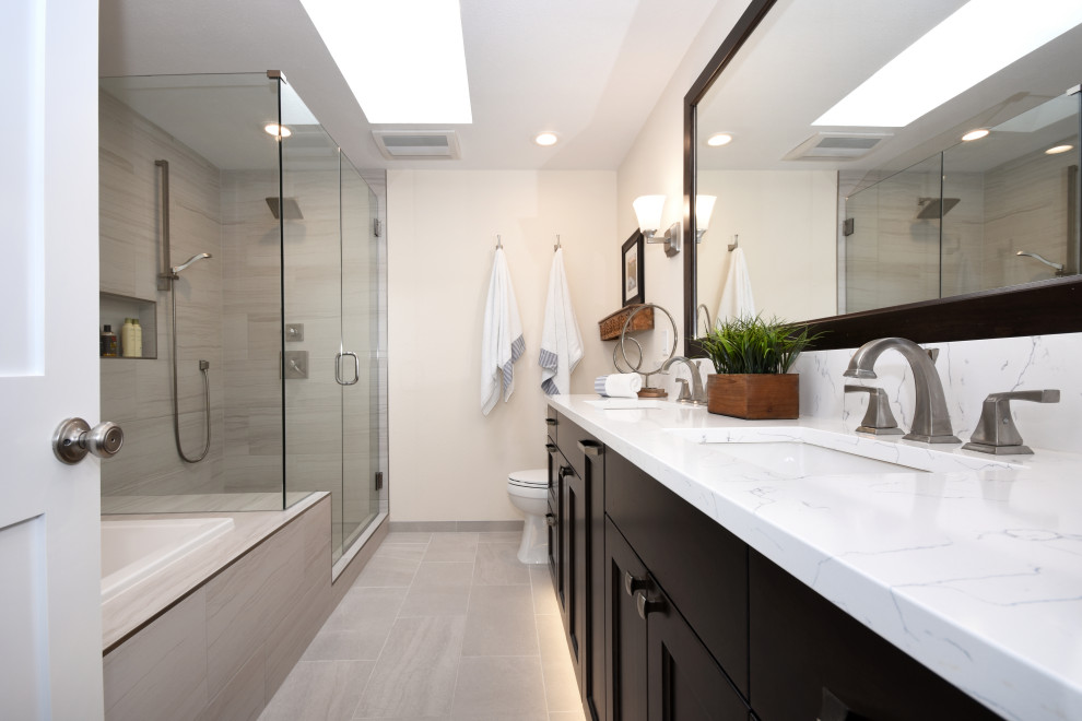 Mid-sized transitional master bathroom in Seattle with shaker cabinets, dark wood cabinets, a drop-in tub, a corner shower, a one-piece toilet, gray tile, porcelain tile, white walls, porcelain floors, an integrated sink, quartzite benchtops, grey floor, a hinged shower door and white benchtops.