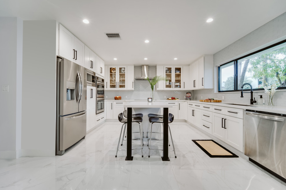 This is an example of a large modern u-shaped eat-in kitchen in Miami with an undermount sink, shaker cabinets, white cabinets, grey splashback, glass tile splashback, stainless steel appliances, ceramic floors, with island, grey floor and white benchtop.