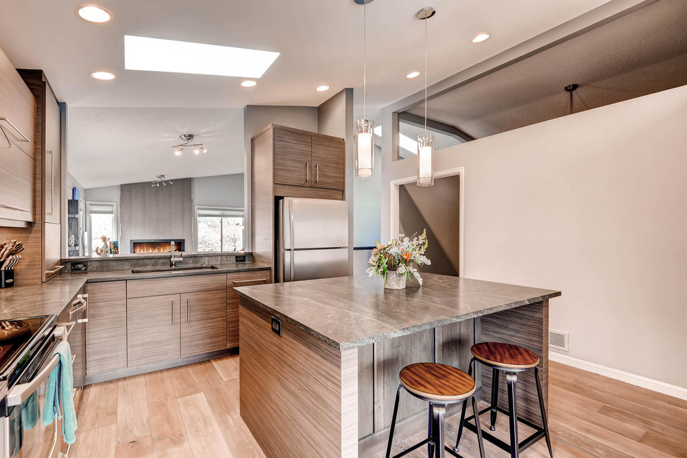 Mid-sized modern l-shaped eat-in kitchen in Denver with an undermount sink, flat-panel cabinets, medium wood cabinets, soapstone benchtops, beige splashback, matchstick tile splashback, stainless steel appliances, light hardwood floors and with island.