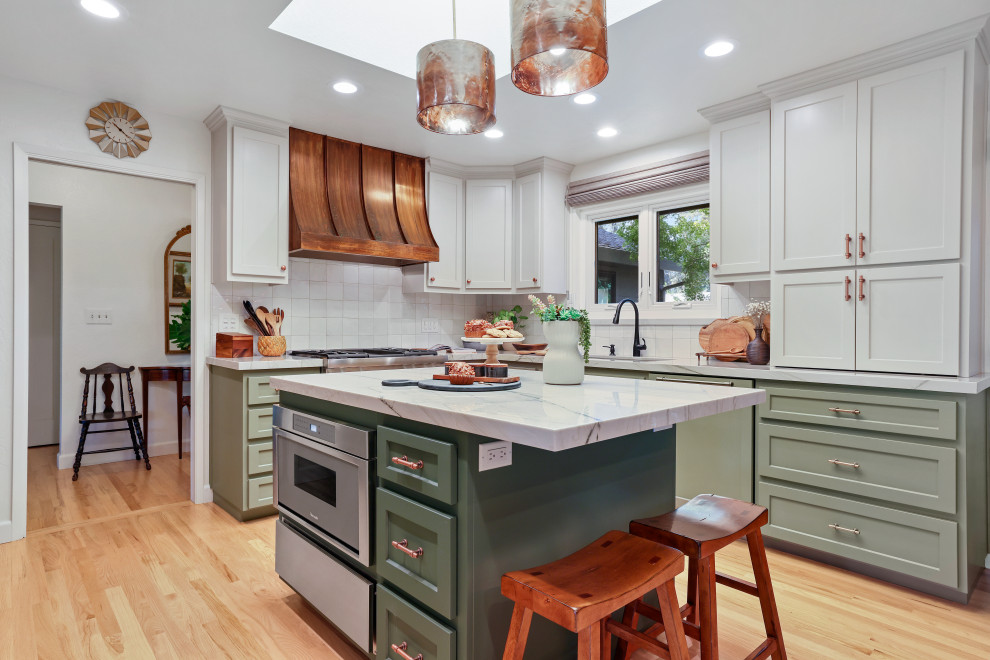 Photo of a transitional l-shaped kitchen in Sacramento with an undermount sink, shaker cabinets, green cabinets, quartzite benchtops, white splashback, ceramic splashback, panelled appliances, with island, light hardwood floors, beige floor and white benchtop.