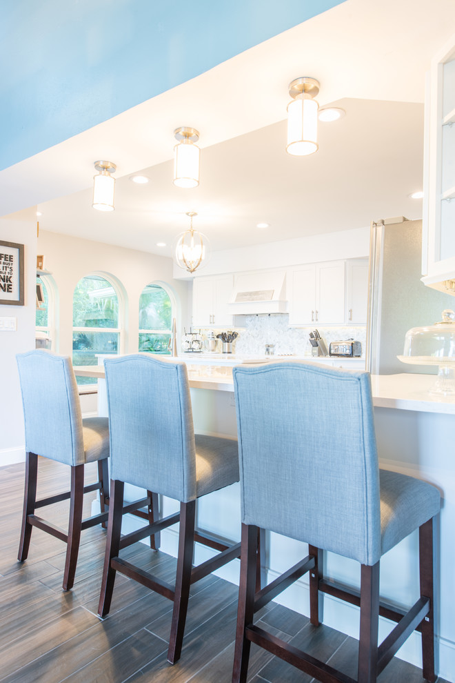 Inspiration for a large transitional u-shaped porcelain tile and brown floor eat-in kitchen remodel with an undermount sink, shaker cabinets, white cabinets, quartz countertops, white backsplash, marble backsplash, stainless steel appliances and two islands