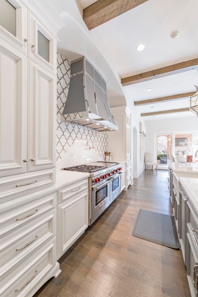 Photo of an expansive transitional l-shaped eat-in kitchen in Dallas with a farmhouse sink, raised-panel cabinets, white cabinets, marble benchtops, multi-coloured splashback, stone tile splashback, stainless steel appliances, dark hardwood floors, multiple islands and brown floor.