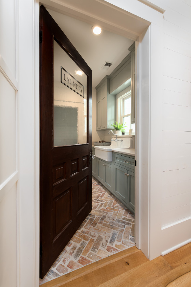 Large country galley dedicated laundry room in Other with a farmhouse sink, flat-panel cabinets, blue cabinets, quartz benchtops, white walls, brick floors, a side-by-side washer and dryer, brown floor and white benchtop.
