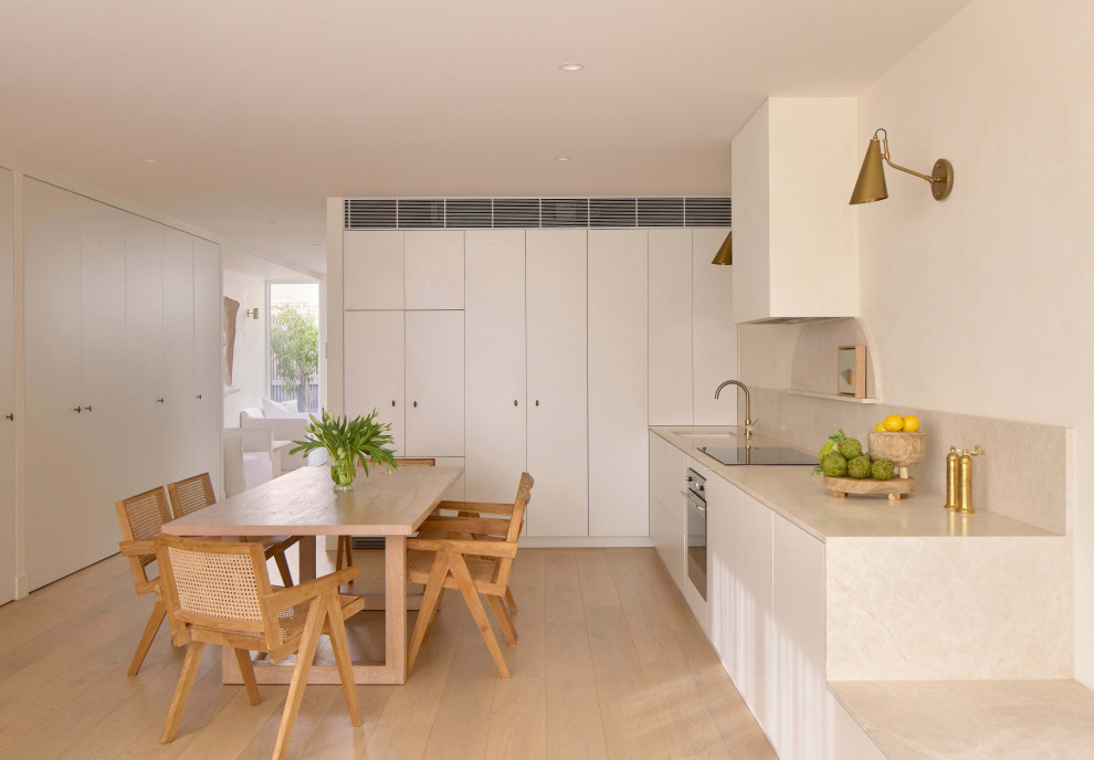 Modern u-shaped eat-in kitchen in Melbourne with an undermount sink, flat-panel cabinets, white cabinets, beige splashback, stone slab splashback, stainless steel appliances, light hardwood floors, beige floor and beige benchtop.