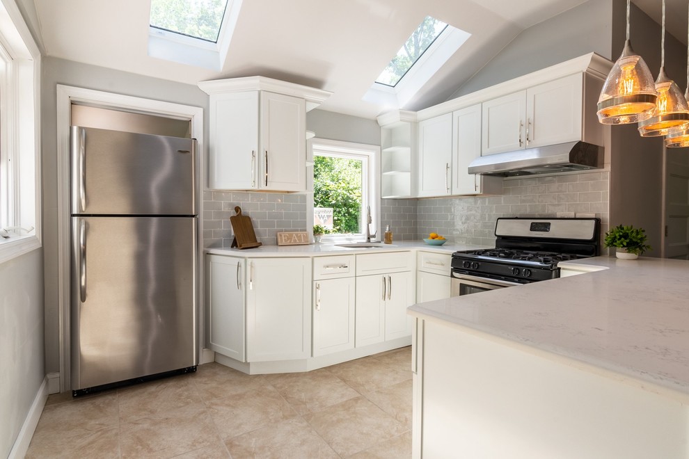 This is an example of a mid-sized modern u-shaped eat-in kitchen in New York with a drop-in sink, white cabinets, granite benchtops, grey splashback, glass tile splashback, stainless steel appliances, with island, beige floor, white benchtop and shaker cabinets.