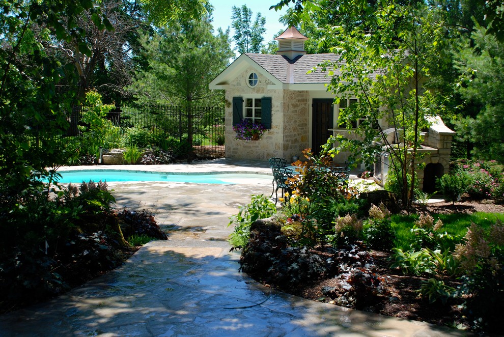 This is an example of a mid-sized traditional backyard kidney-shaped lap pool in Toronto with a pool house and natural stone pavers.