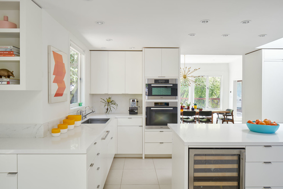 Inspiration for a midcentury l-shaped kitchen in San Francisco with a double-bowl sink, flat-panel cabinets, white cabinets, white splashback, stainless steel appliances and with island.